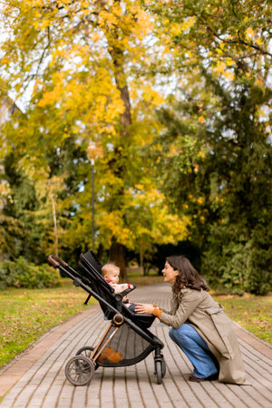Young woman with a cute baby girl in baby stroller at the autumn park