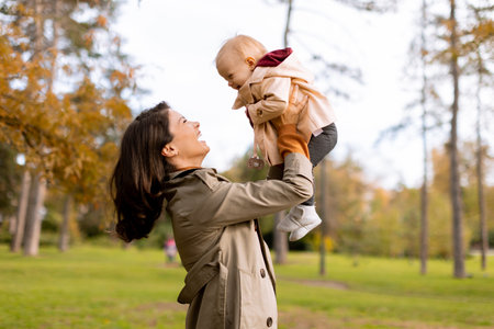 Young woman holding a cute baby girl in the autumn parkの写真素材