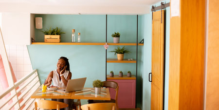 Aoung African american woman working on a laptop and having a healthy breakfast in the cafeの写真素材