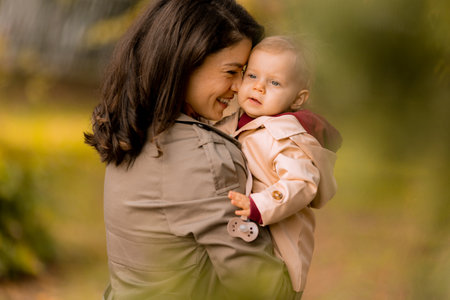 Young woman holding a cute baby girl in the autumn parkの写真素材