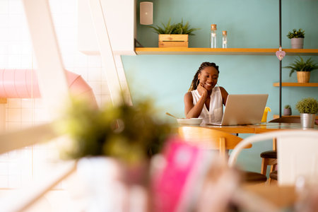 Aoung African american woman working on a laptop and having a healthy breakfast in the cafeの写真素材