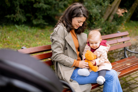 Young woman sitting on a bench with a cute baby girl in the autumn parkの写真素材