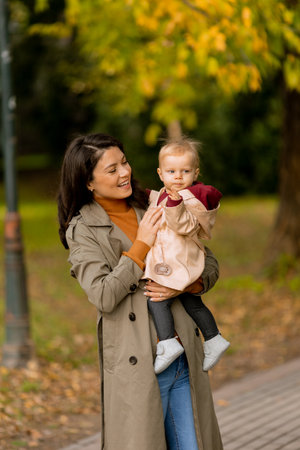 Young woman holding a cute baby girl in the autumn parkの写真素材