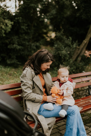 Young woman sitting on a bench with a cute baby girl in the autumn parkの写真素材