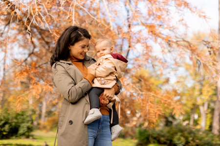 Young woman holding a cute baby girl in the autumn parkの写真素材