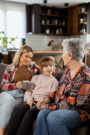 Three generations of women enjoy laughter and conversation on a comfortable living room couchの写真素材