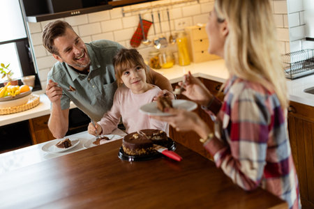 A heartwarming scene unfolds as a family relishes a mouthwatering chocolate cake together in the warmth of their sunlit kitchen, sharing smiles and creating memoriesの写真素材