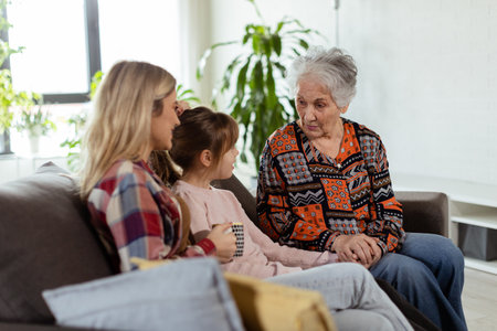 Three generations of women enjoy laughter and conversation on a comfortable living room couchの写真素材