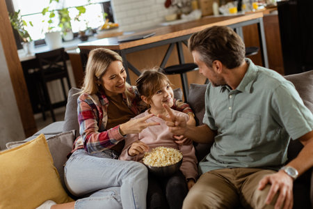 A joyful family lounges on the sofa, engaging in playful conversation with a bowl of popcornの写真素材