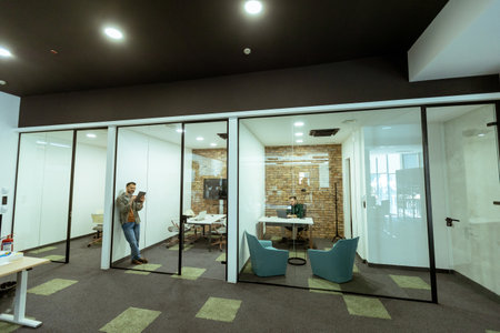 Person is immersed in a task in a stylish office with transparent glass walls. The modern design includes exposed brick, a sleek monitor, comfortable seating, and an atmosphere of quiet productivity. This scene captures a moment of dedicated work in a contemporary urban workspace.の写真素材