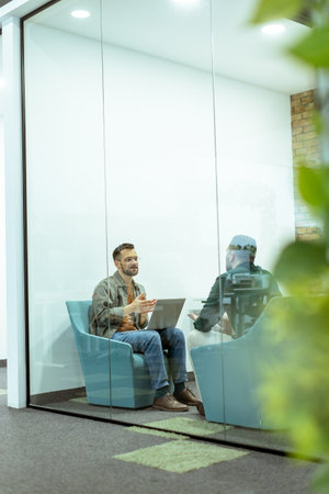 Two professionals engage in a conversation while seated comfortably in an office lounge, surrounded by greenery and contemporary design elementsの写真素材