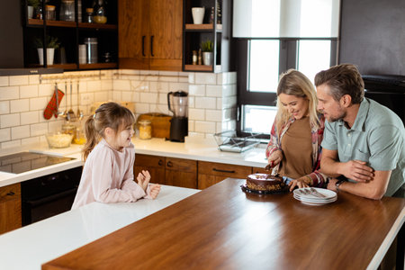 A heartwarming scene unfolds as a family relishes a mouthwatering chocolate cake together in the warmth of their sunlit kitchen, sharing smiles and creating memoriesの写真素材