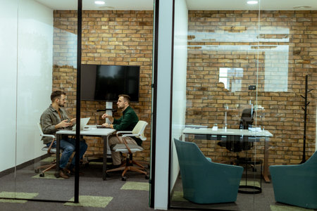 Two professionals engage in a conversation while seated comfortably in an office lounge, surrounded by greenery and contemporary design elementsの写真素材