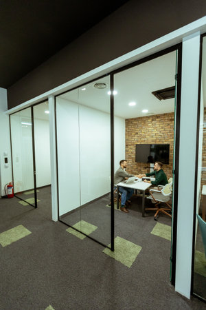 Two professionals engage in a conversation while seated comfortably in an office lounge, surrounded...