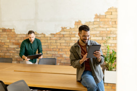 In a contemporary office setting, two focused colleagues engage in their work with tablet and laptop, collaborating and sharing ideas in a bright and casual environment.の写真素材