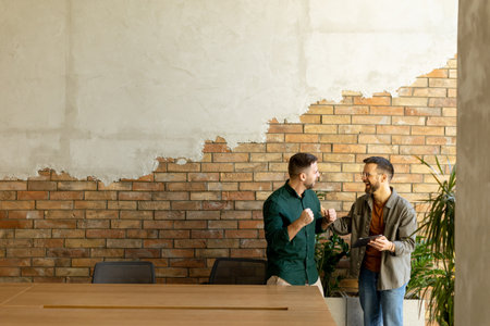 Two professionals are engaged in a focused conversation while holding digital tablet in a contemporary office space, featuring rustic exposed brickwork and warm natural lightの写真素材