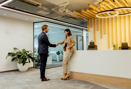 Two professionals exchanging greetings with a friendly handshake in a sleek office environmentの写真素材