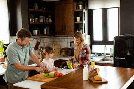 Man cuts bell peppers as a child observes, with a woman sipping orange juice in the backgroundの写真素材
