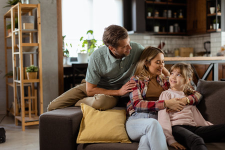 Joyful family shares a relaxed, affectionate moment on the sofa, illuminated by soft natural lightの写真素材