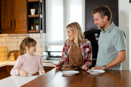 A heartwarming scene unfolds as a family relishes a mouthwatering chocolate cake together in the warmth of their sunlit kitchen, sharing smiles and creating memoriesの写真素材