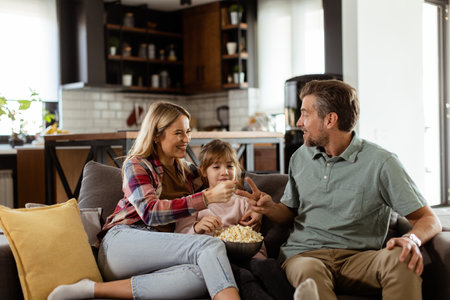 A joyful family lounges on the sofa, engaging in playful conversation with a bowl of popcornの写真素材