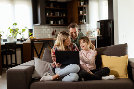 Joyful family of three spends quality time together on the living room sofa, sharing a moment around a laptop in their comfortable homeの写真素材