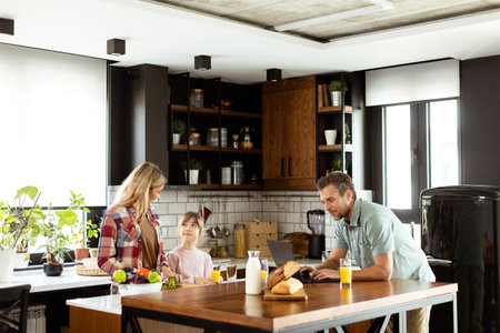Young family chatting and preparing food around a bustling kitchen counter filled with fresh ingredients and cooking utensilsの写真素材