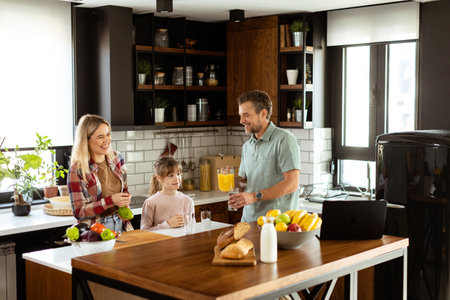 Young family chatting and preparing food around a bustling kitchen counter filled with fresh ingredients and cooking utensilsの写真素材