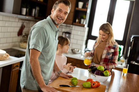 Man cuts bell peppers as a child observes, with a woman sipping orange juice in the backgroundの写真素材