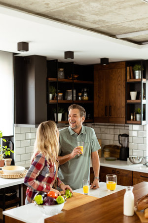 A pair enjoying a lighthearted conversation with fresh juice and a healthy breakfast spread on the counter.の写真素材