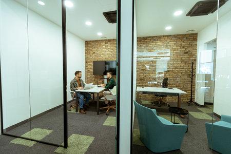 Two professionals engage in a conversation while seated comfortably in an office lounge, surrounded by greenery and contemporary design elementsの写真素材