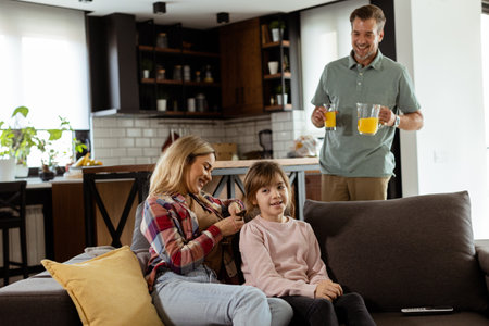 A smiling father brings a tray of orange juice to his happy family seated in a living roomの写真素材