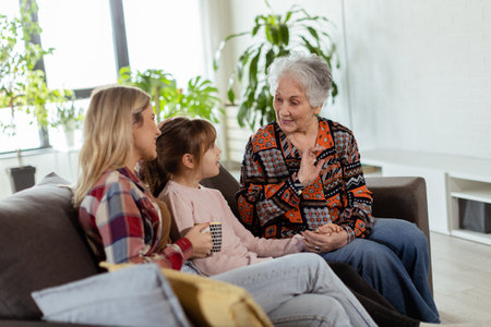 Three generations of women enjoy laughter and conversation on a comfortable living room couchの写真素材