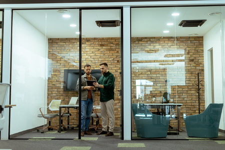 Two professionals engage in a conversation while standing in an office lounge, surrounded by contemporary design elementsの写真素材