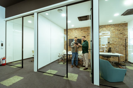 Two professionals engage in a conversation while standing in an office lounge, surrounded by contemporary design elementsの写真素材