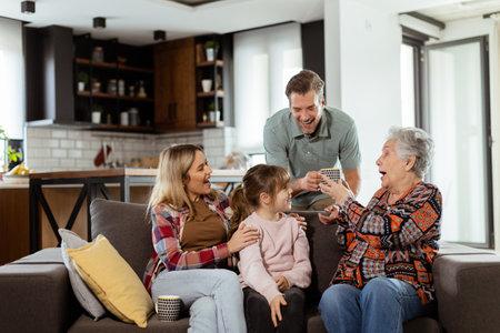 Heartwarming scene unfolds as a multi-generational family gathers on a couch to present a birthday cake to a delighted grandmother, creating memories to cherishの写真素材