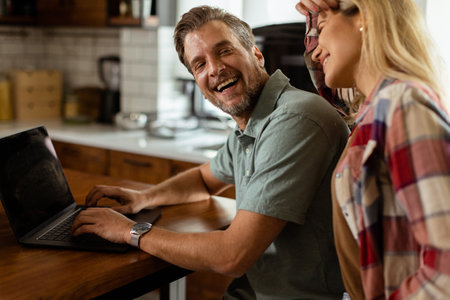 A cheerful couple enjoys a light-hearted moment in their sunny kitchen, working on laptop surrounded by a healthy breakfastの写真素材