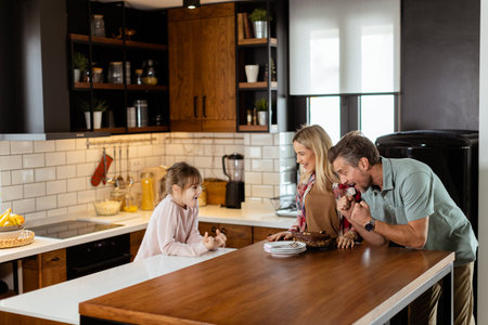 A heartwarming scene unfolds as a family relishes a mouthwatering chocolate cake together in the warmth of their sunlit kitchen, sharing smiles and creating memoriesの写真素材