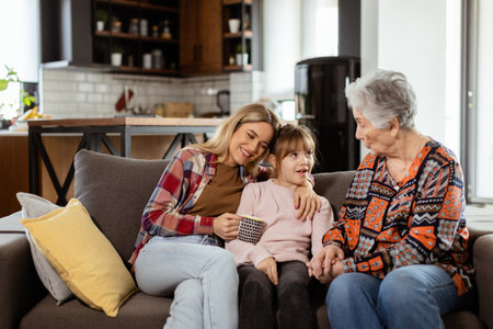 Three generations of women enjoy laughter and conversation on a comfortable living room couchの写真素材
