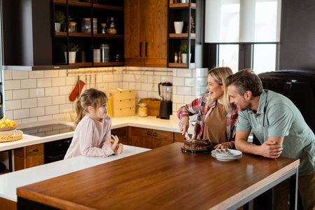 A heartwarming scene unfolds as a family relishes a mouthwatering chocolate cake together in the warmth of their sunlit kitchen, sharing smiles and creating memoriesの写真素材