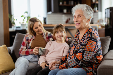 Three generations of women enjoy laughter and conversation on a comfortable living room couchの写真素材