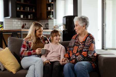 Three generations of women enjoy laughter and conversation on a comfortable living room couchの写真素材