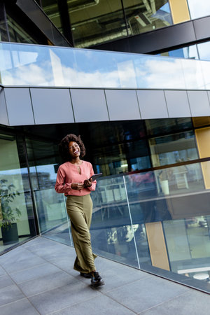 A woman stands confidently outside a contemporary building, tablet in hand, looking towards the future.の写真素材