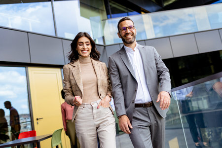 Two professionals exude confidence and happiness as they walk out of a contemporary office, reflecting success.の写真素材