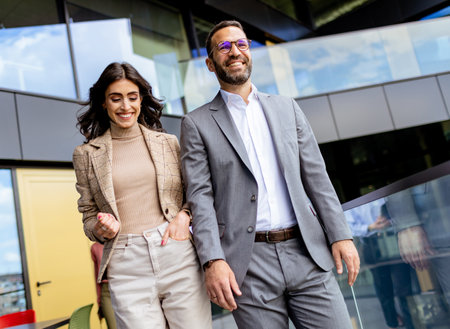 Two professionals exude confidence and happiness as they walk out of a contemporary office, reflecting success.の写真素材