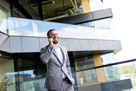 Suited man with arms crossed stands proudly before a sleek building, reflecting ambition.の写真素材