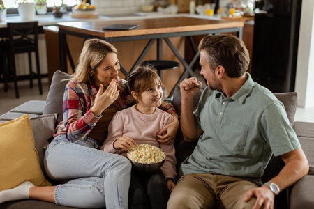 A joyful family lounges on the sofa, engaging in playful conversation with a bowl of popcornの写真素材