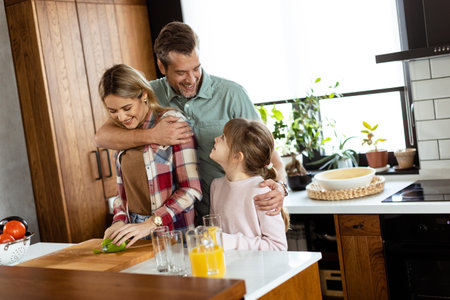 Young family chatting and preparing food around a bustling kitchen counter filled with fresh ingredients and cooking utensilsの写真素材
