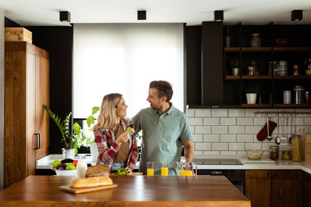 A happy couple enjoys a casual conversation with morning drinks in their sunny kitchen.の写真素材