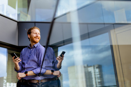 A focused man in a striped shirt talks on his phone while overlooking the balcony at bathed in sunlight.の写真素材